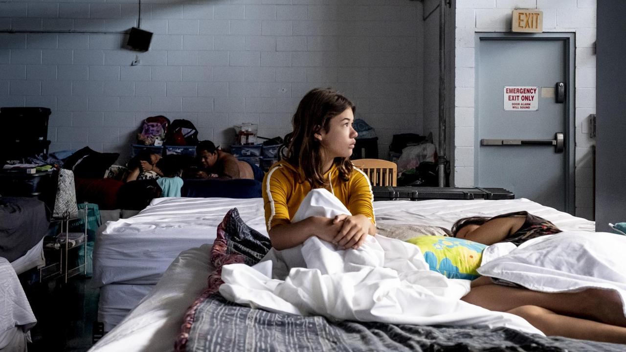 Ein Mädchen sitzt in einem Bett in einer Notunterkunft. 