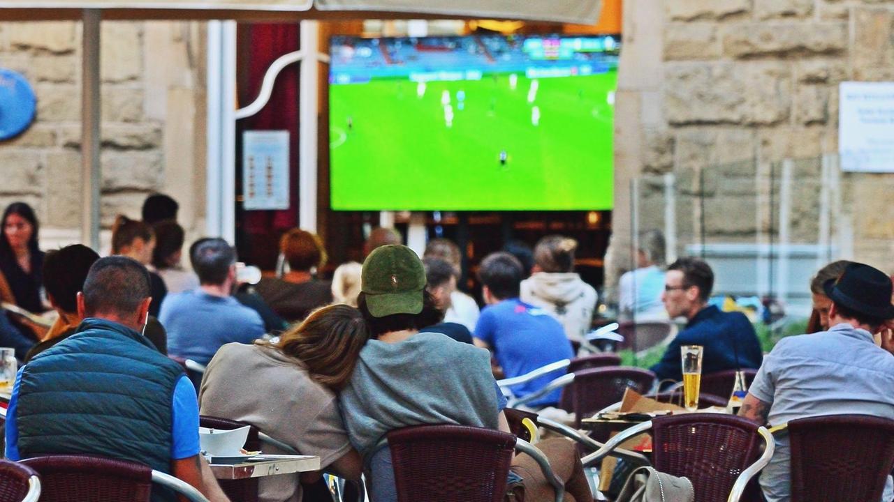 Fußballfans sitzen in einem Café. Sie schauen ein EM-Spiel von der deutschen Mannschaft