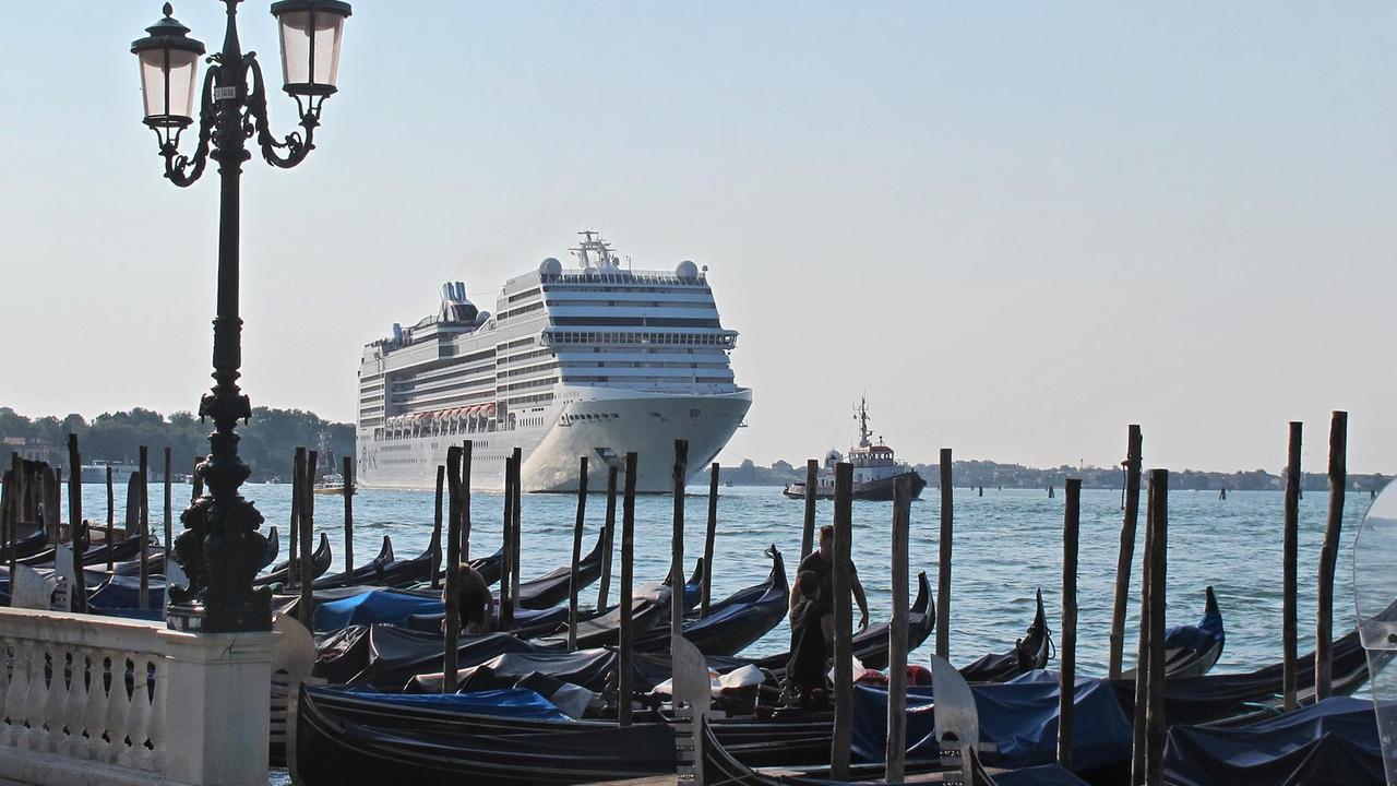 Ein riesiges Kreuzfahrtschiff fährt an venezianischen Gondel vorbei.
