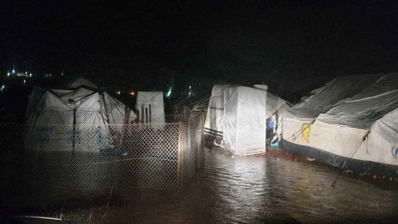 Weiße Zelte stehen nachts bei Regen tief im Wasser.