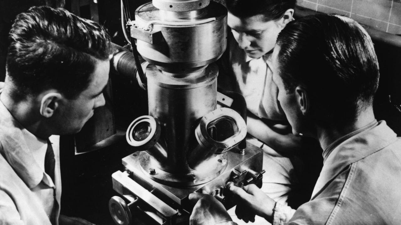 Eine Forscherin und ein Forschung sitzen um ein Elektronenmikroskop, um 1935/40 