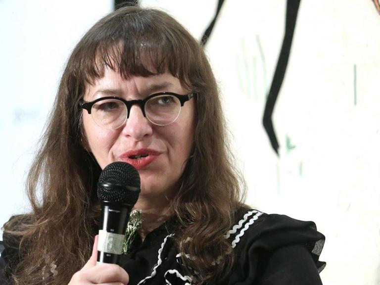 Comiczeichnerin Ulli Lust sitzt auf eine Podium. Eine Frau mit langen dunklen Haaren und einer Brille.