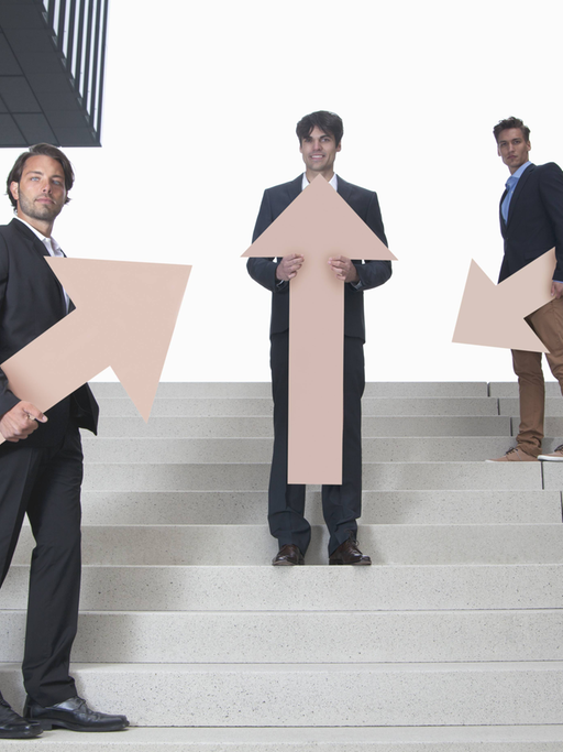 Drei junge Männer stehen mit Pfeilen, die in unterschiedliche Richtungen weisen, auf einer Treppe.