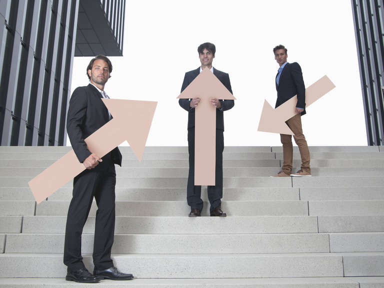 Drei junge Männer stehen mit Pfeilen, die in unterschiedliche Richtungen weisen, auf einer Treppe.