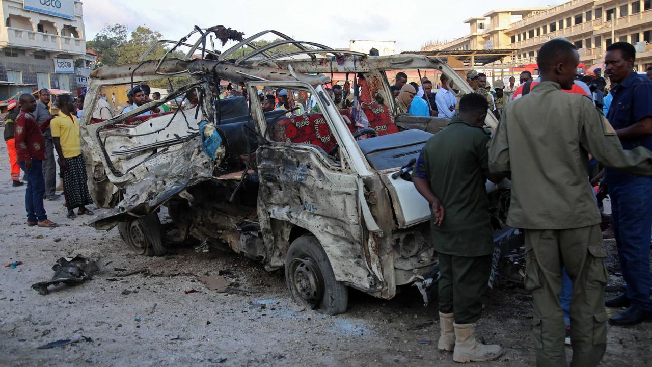 Sicherheitskräfte schauen in Mogadischu auf das Wrack eines explodierten Kleinbusses.