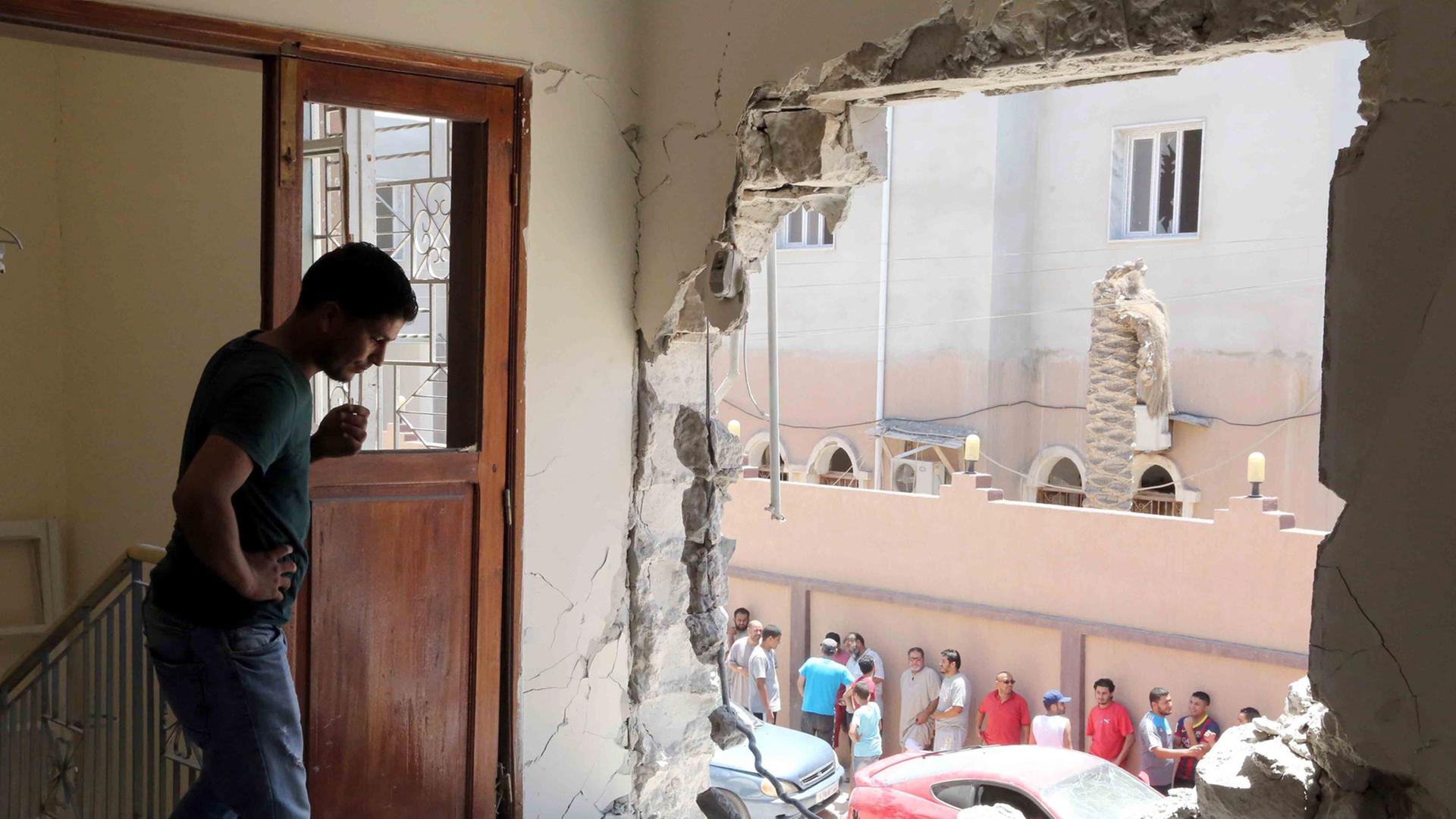 Ein Mann schaut nach dem Einschlag einer Granate durch die zerstörte Wand seiner Wohnung.