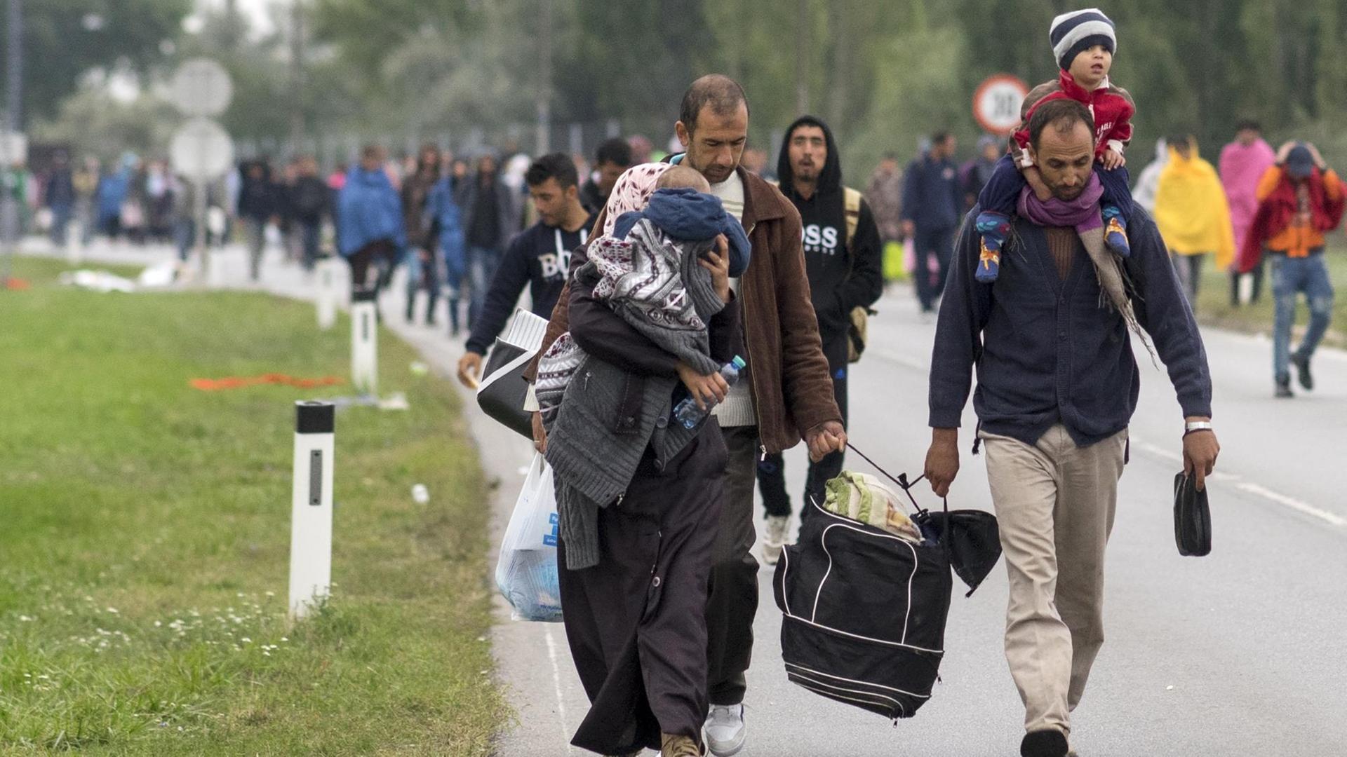 Flüchtlinge laufen mit Kindern auf dem Arm und Gepäck in der Hand auf einer Straße.