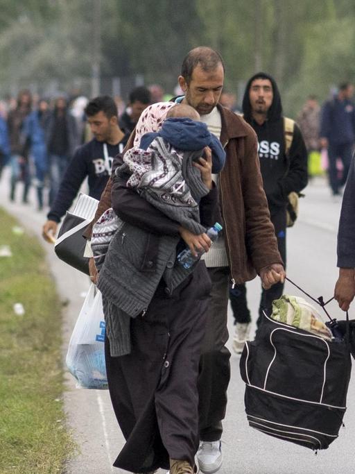 Flüchtlinge laufen mit Kindern auf dem Arm und Gepäck in der Hand auf einer Straße.