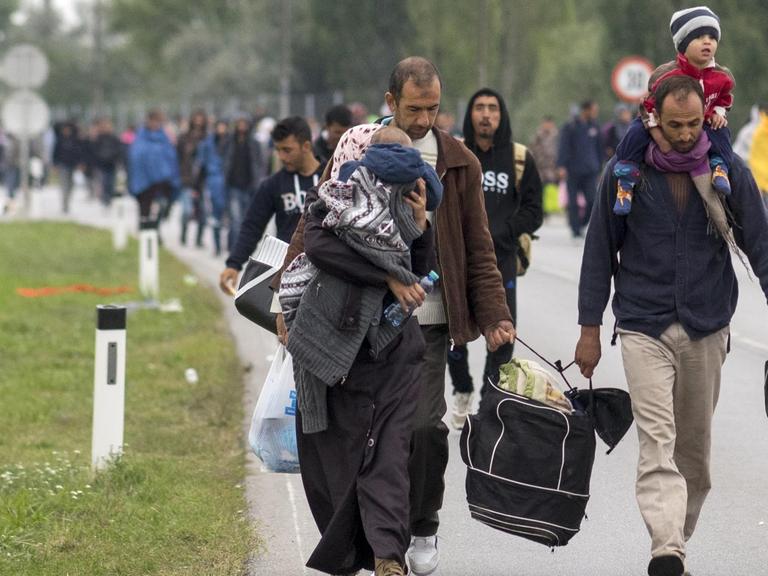 Flüchtlinge laufen mit Kindern auf dem Arm und Gepäck in der Hand auf einer Straße.