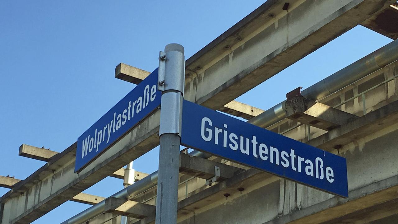 Straßenschilder "Wolpylastraße" und "Grisutenstraße" vor einem Industriegebäude.