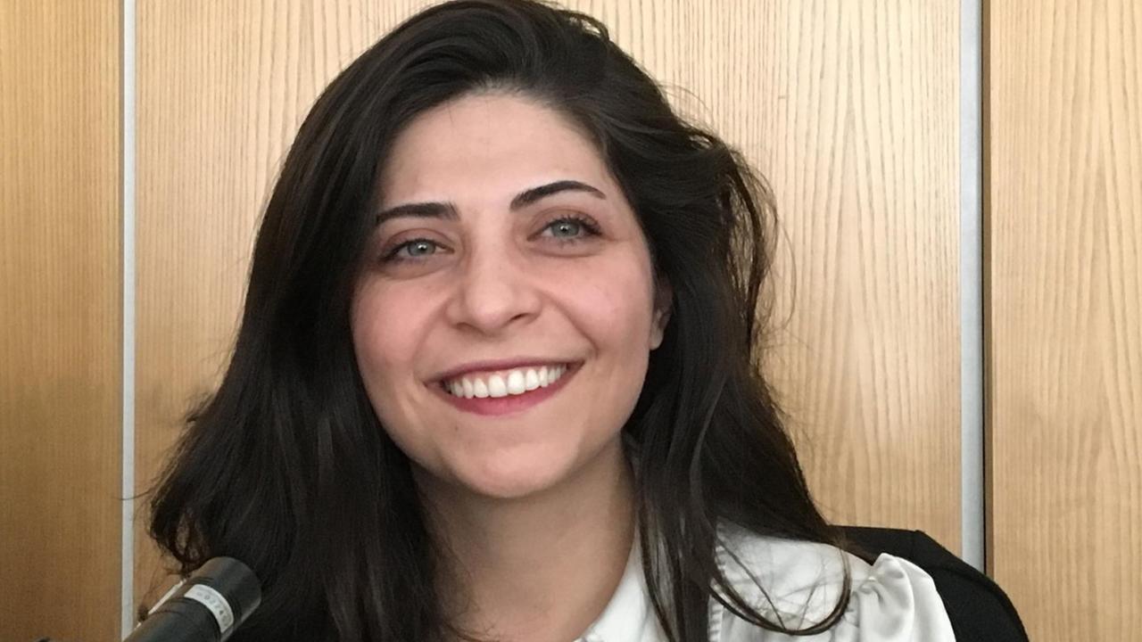 Shadi Adib  sitzt vor einem Mikrofon und lacht in die Kamera.