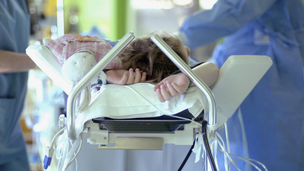 Eine Kind, auf einer Krankenhausliege wird vom medizinischen Personal überwacht.