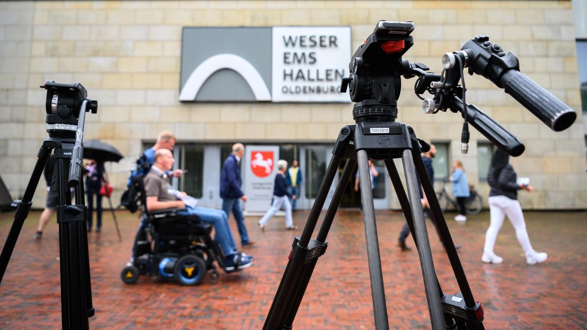 Personen sind während des letzten Prozesstages des Patientenmörders Niels Högel vor der Weser-Ems-Halle hinter zwei Filmstativen.