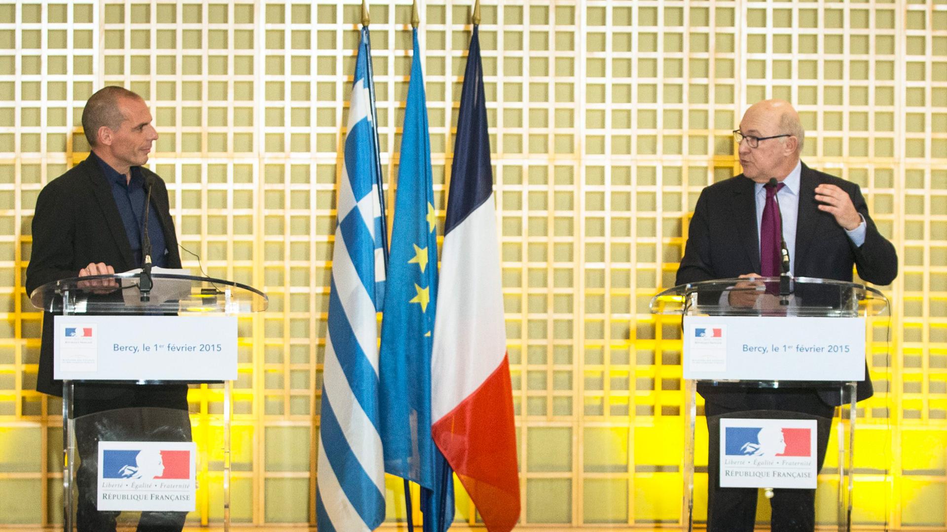 Yannis Varoufakis und Michel Sapin sprechen an Stehpulten bei einer Pressekonferenz, zwischen ihnen die Flaggen beider Länder und die der EU.