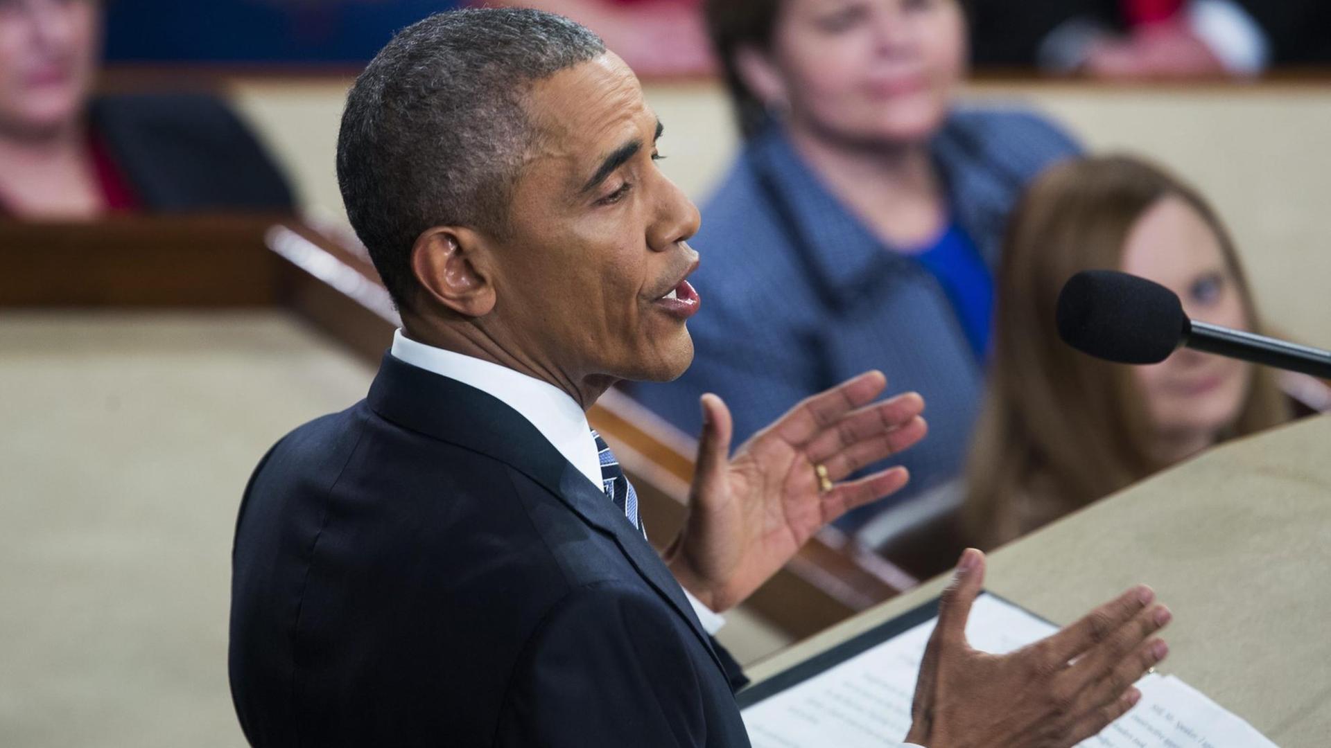 Obama steht am Rednerpult, von schräg hinten fotografiert.