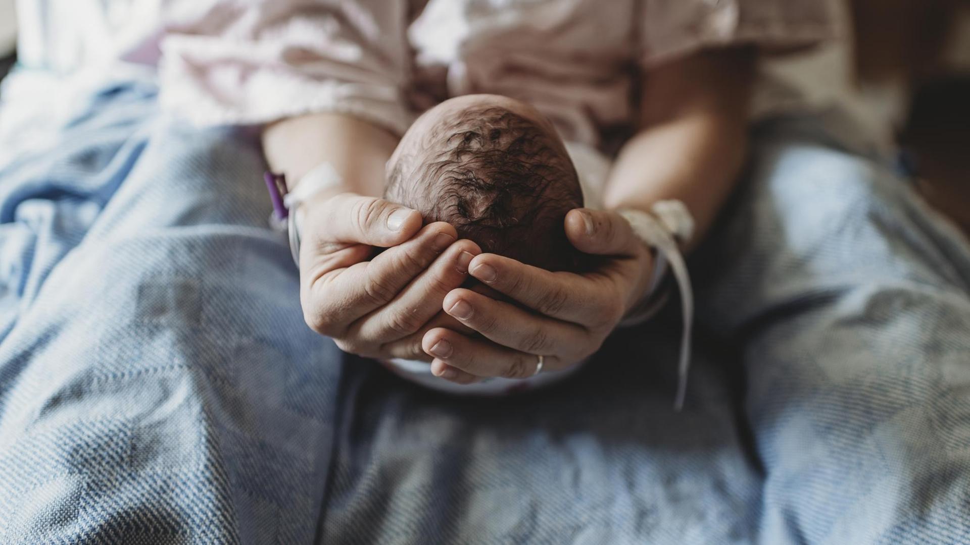 Eine Frau hält den Kopf eines Neugeborenen in den Händen.