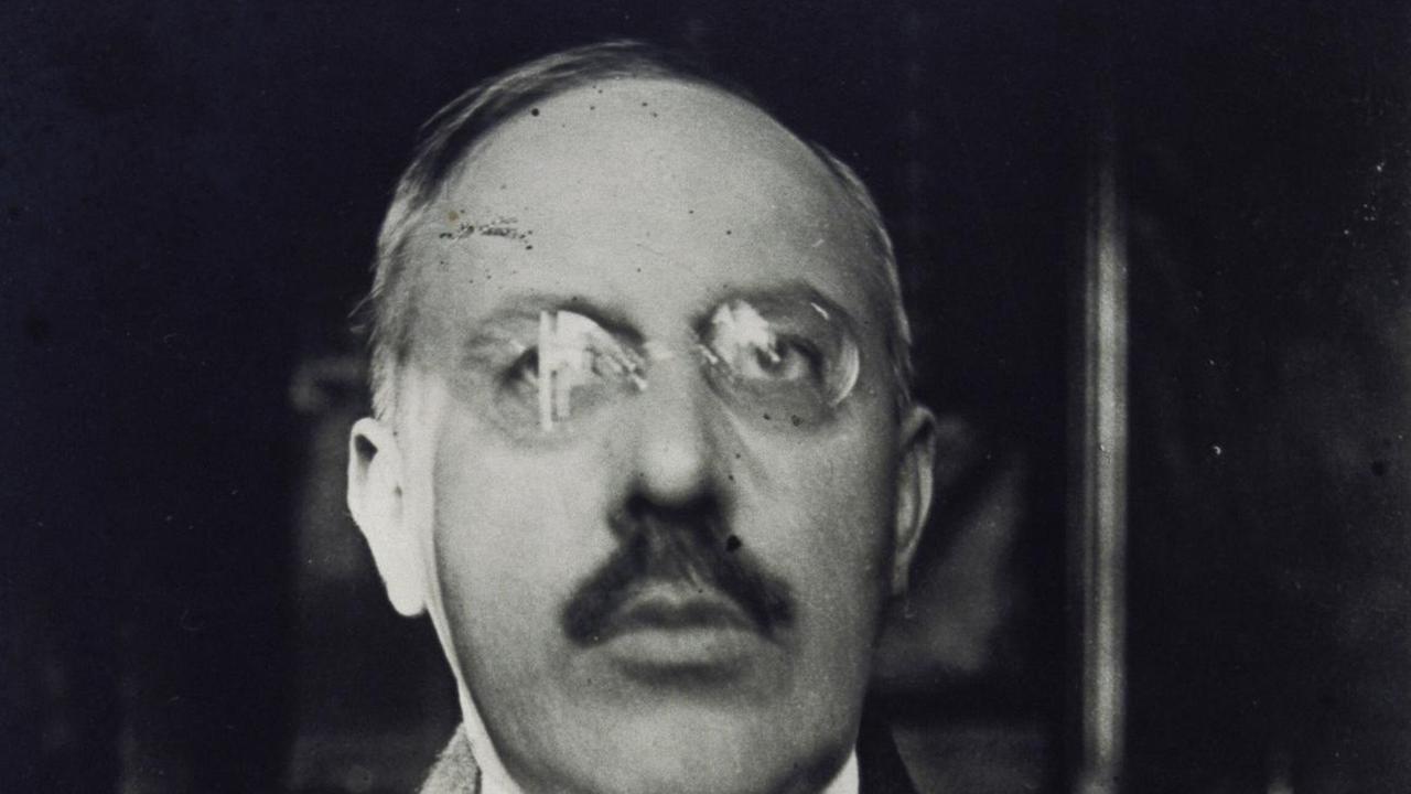 Schwarz-Weiß-Fotografie von ca. 1915 des österreichischern Architekten Josef Hoffmann (1870- 1956 in Anzug mit Krawatte Brille und großem Schnäuzer.