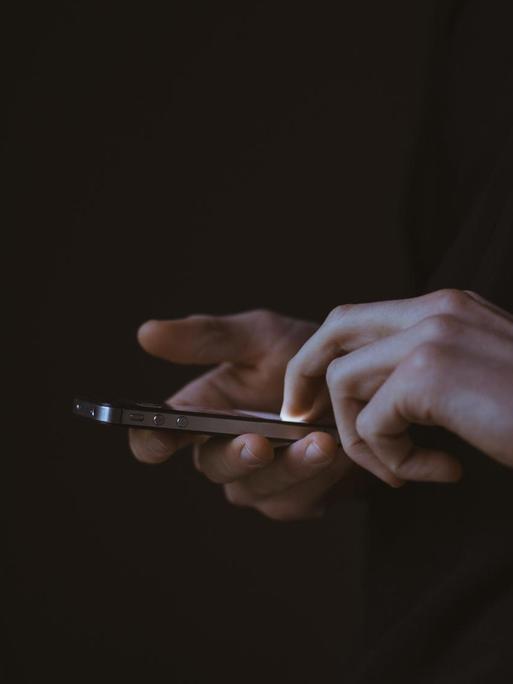 Eine Person hält im Dunklen ein Smartphone in der Hand, das Display leuchtet.
