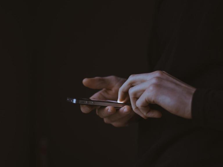 Eine Person hält im Dunklen ein Smartphone in der Hand, das Display leuchtet.