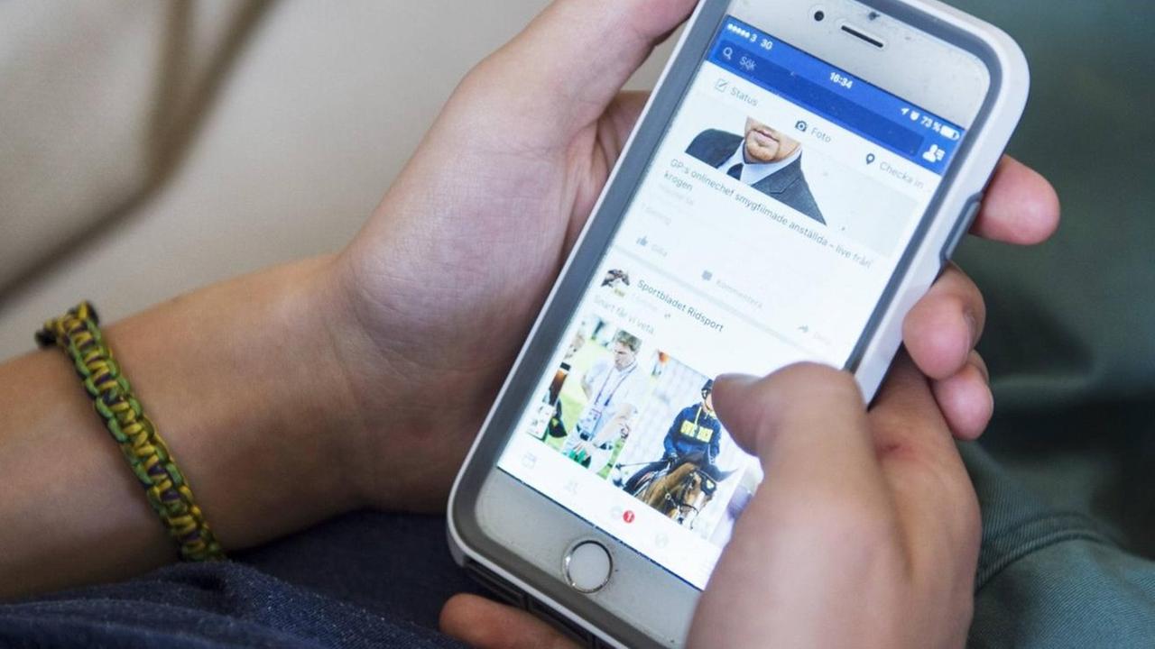 Ein Junge surft auf seinem Smartphone bei Facebook.