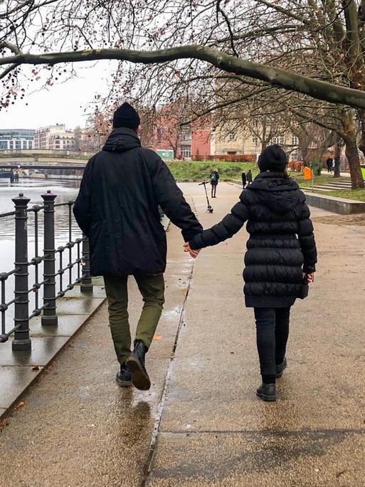 Ein Mann und deine Frau gehen Hand in Hand am Spree Ufer in Berlin spazieren.