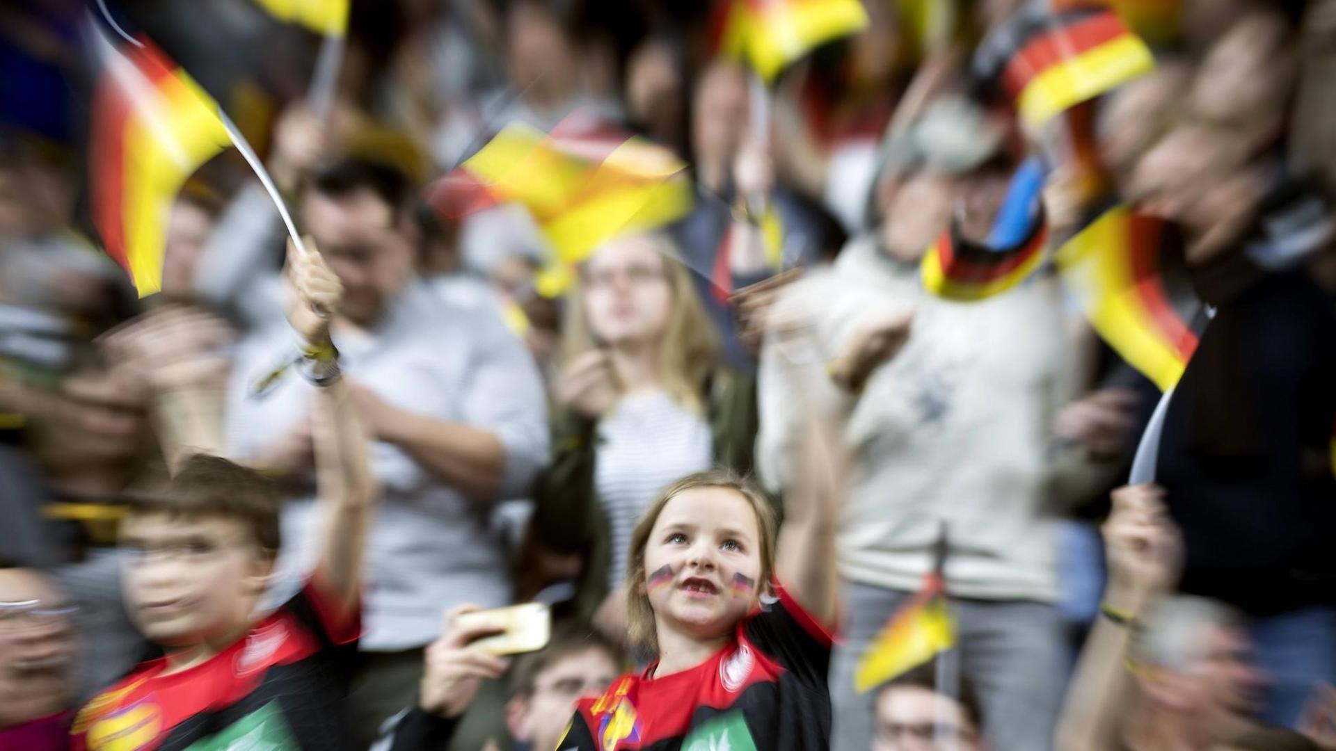 Ein verschwommenes Bild mit Zuschauern mit Deutschlandfähnchen in der Hand.