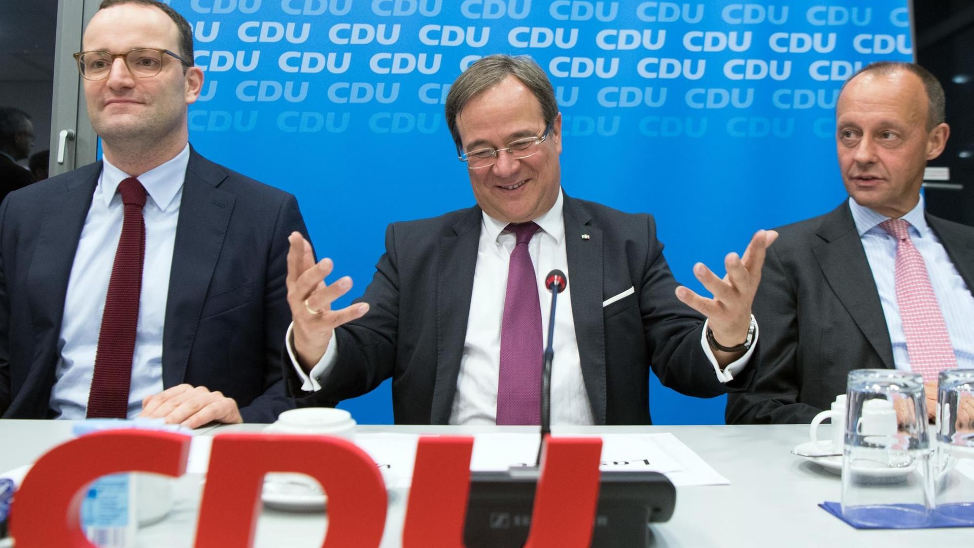 Jens Spahn, Armin Laschet und Friedrich Merz sitzen an einem Tisch vor und hinter CDU-Parteilogos.