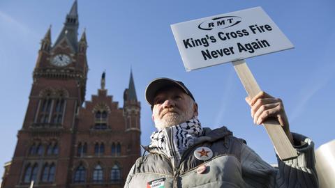 Ein Mann mit einem Schild mit der Aufschrfit "King's Cross Fire Never Again" steht vor dem King's Cross Bahnhof in London