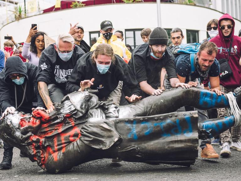 Demonstranten schieben die Statur von Edward Colston richtung Wasser.
