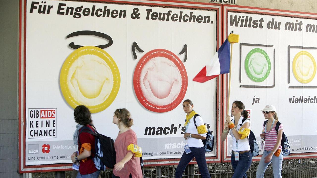 Teilnehmer des 20. katholischen Weltjugendtages spazieren am Mittwoch, 17.08.05, in der Kölner Innenstadt an einer Kondomwerbung vorbei. | Verwendung weltweit