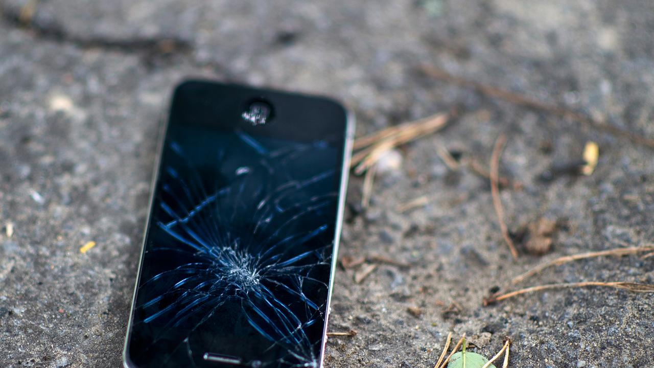 Ein schwarzes Mobiltelefon liegt mit zersplittertem Display auf dem Boden.