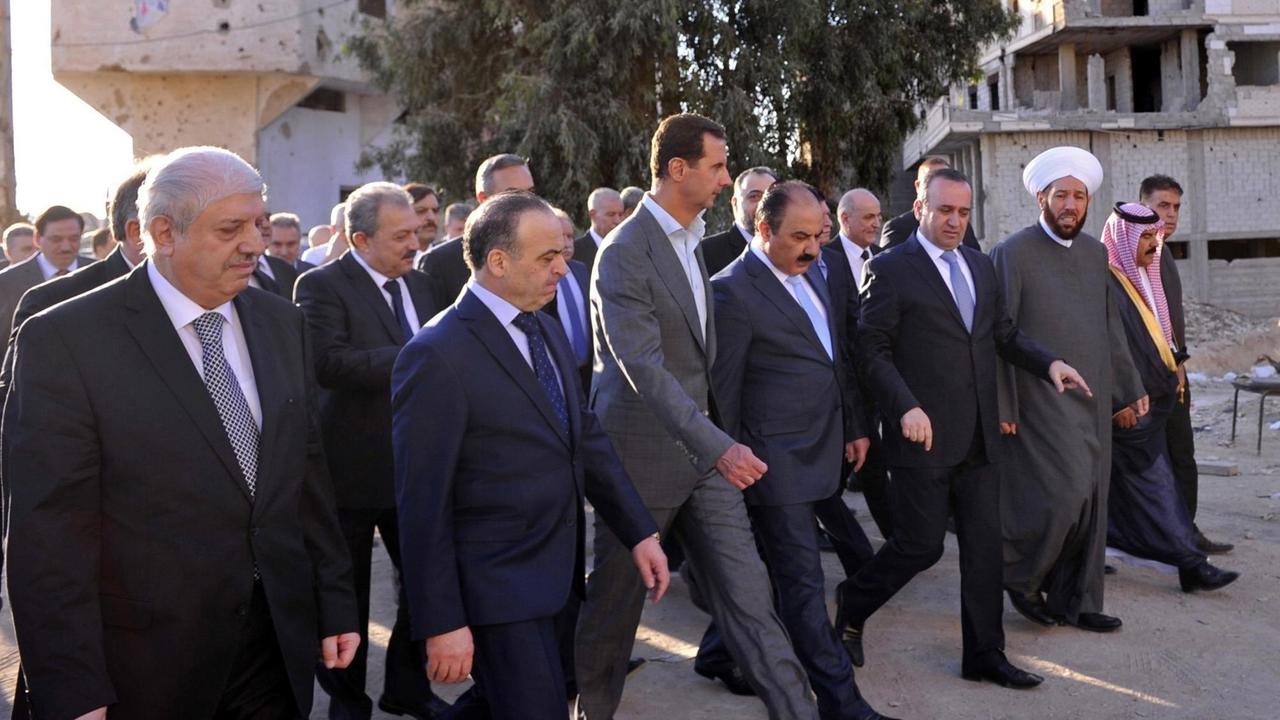Ein Foto der staatlichen syrischen Nachrichtenagentur Sana zeigt den syrischen Machthaber Baschar al-Assad, wie er in einer Gruppe durch die syrische Stadt Daraja läuft.