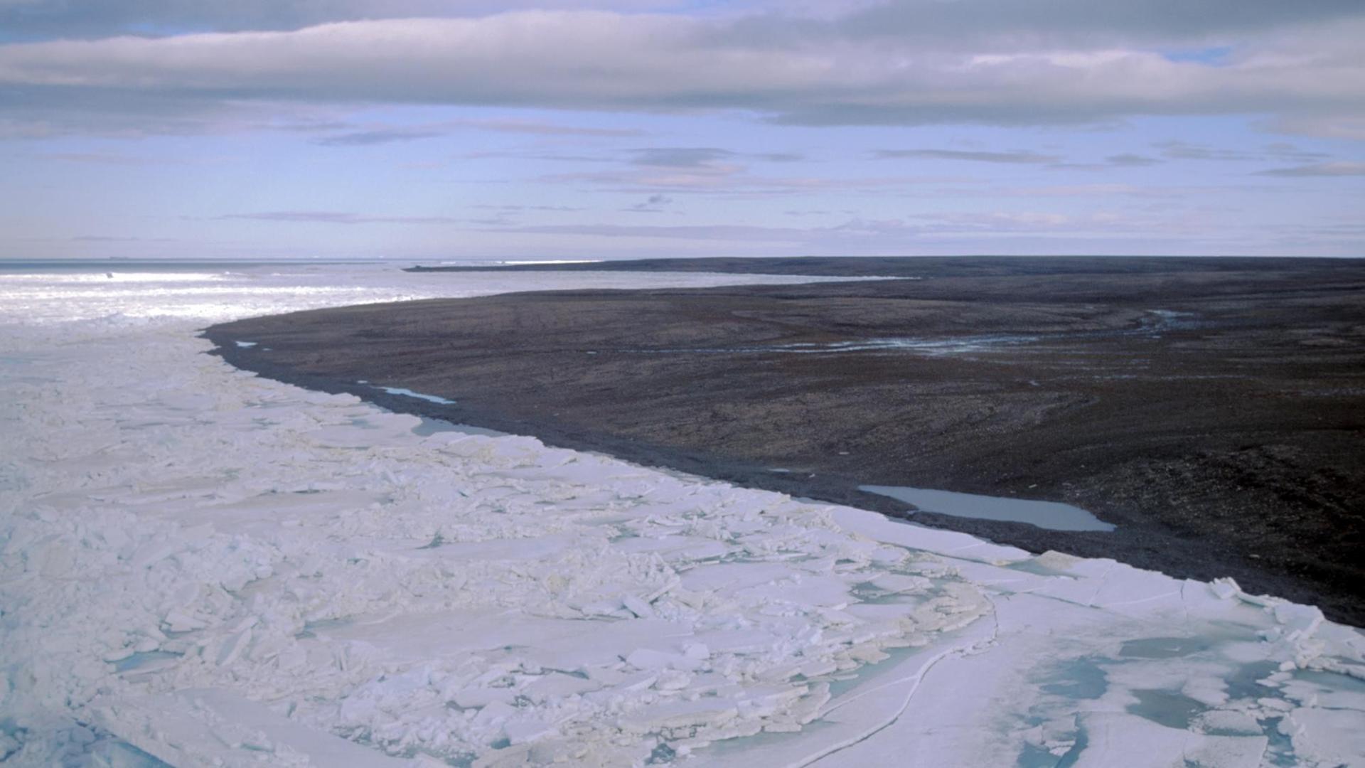 Blick auf die zu Russland gehörende Bolschewik-Insel. Im Vordergrund Packeis, im Hintergrund ist die Landschaft schon aufgetaut und schlammig.