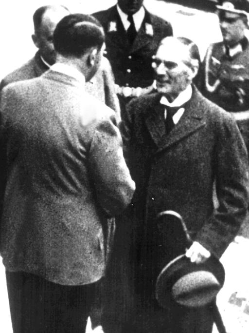 Adolf Hitler, ein paar Stufen über Arthur Neville Chamberlain stehend, schüttelt ihm die Hand