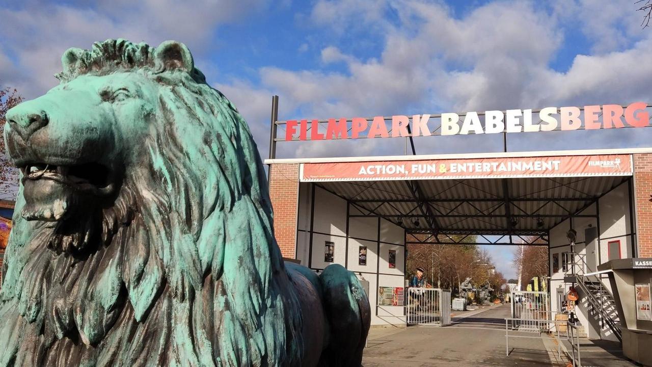 Das Eingangstor des Filmparks Babelsberg. Links im Bildvordergrund eine Löwenskulptur.