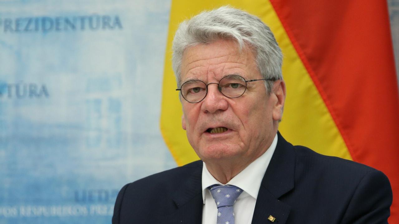 Joachim Gauck an einem Rednerpult mit Mikrofon, hinter ihm die deutsche Flagge