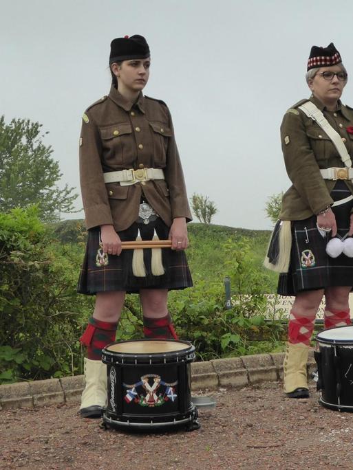Ein Mann, zwei junge Frauen und ein Mädchen stehen mit Trommeln und schottischer Tracht nebeneinander