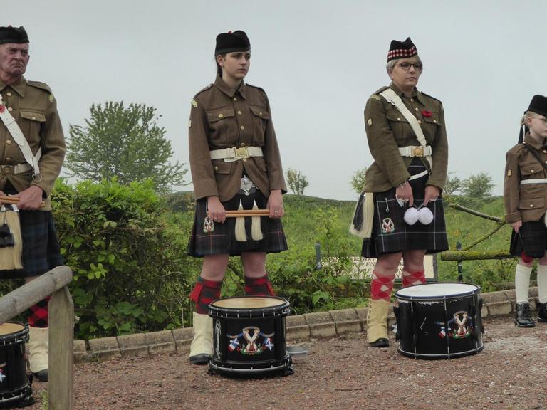Ein Mann, zwei junge Frauen und ein Mädchen stehen mit Trommeln und schottischer Tracht nebeneinander