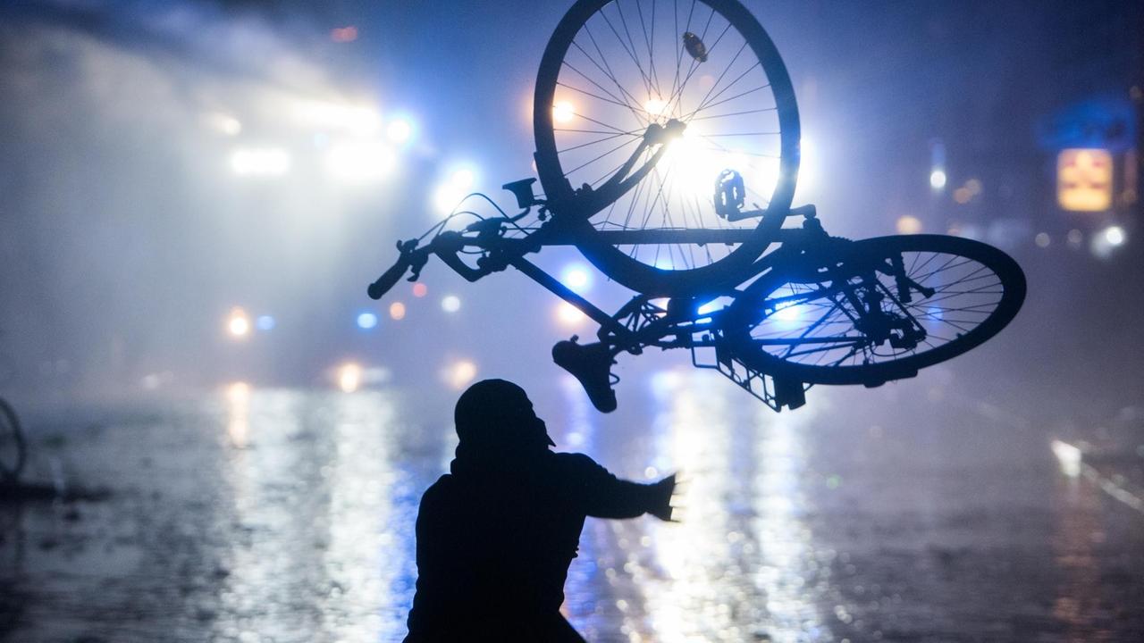 Ein Randalierer wirft im Schanzenviertel ein Fahrrad in Richtung von Wasserwerfern. 