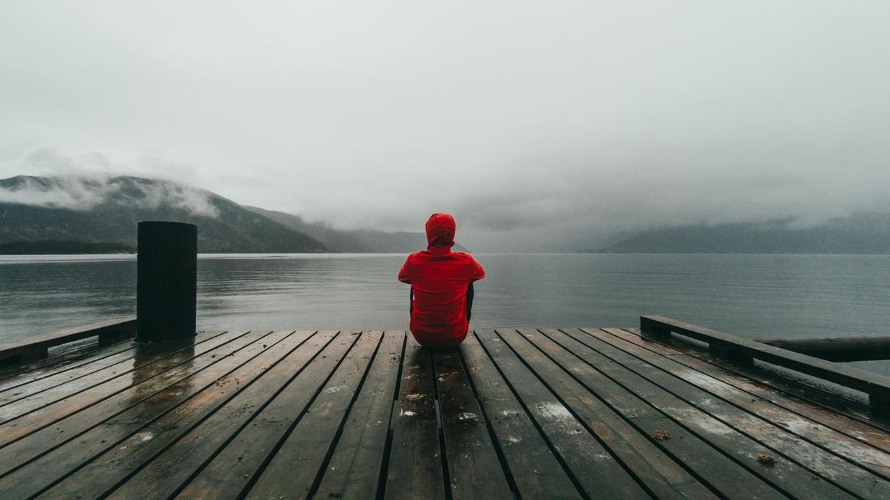 Ein Mann sitzt auf einem Steg eines Sees und blickt auf das Wasser.