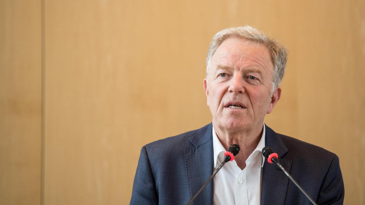 Martin Schairer spricht in zwei Mikrofonen vor einem beigen Hintergrund.