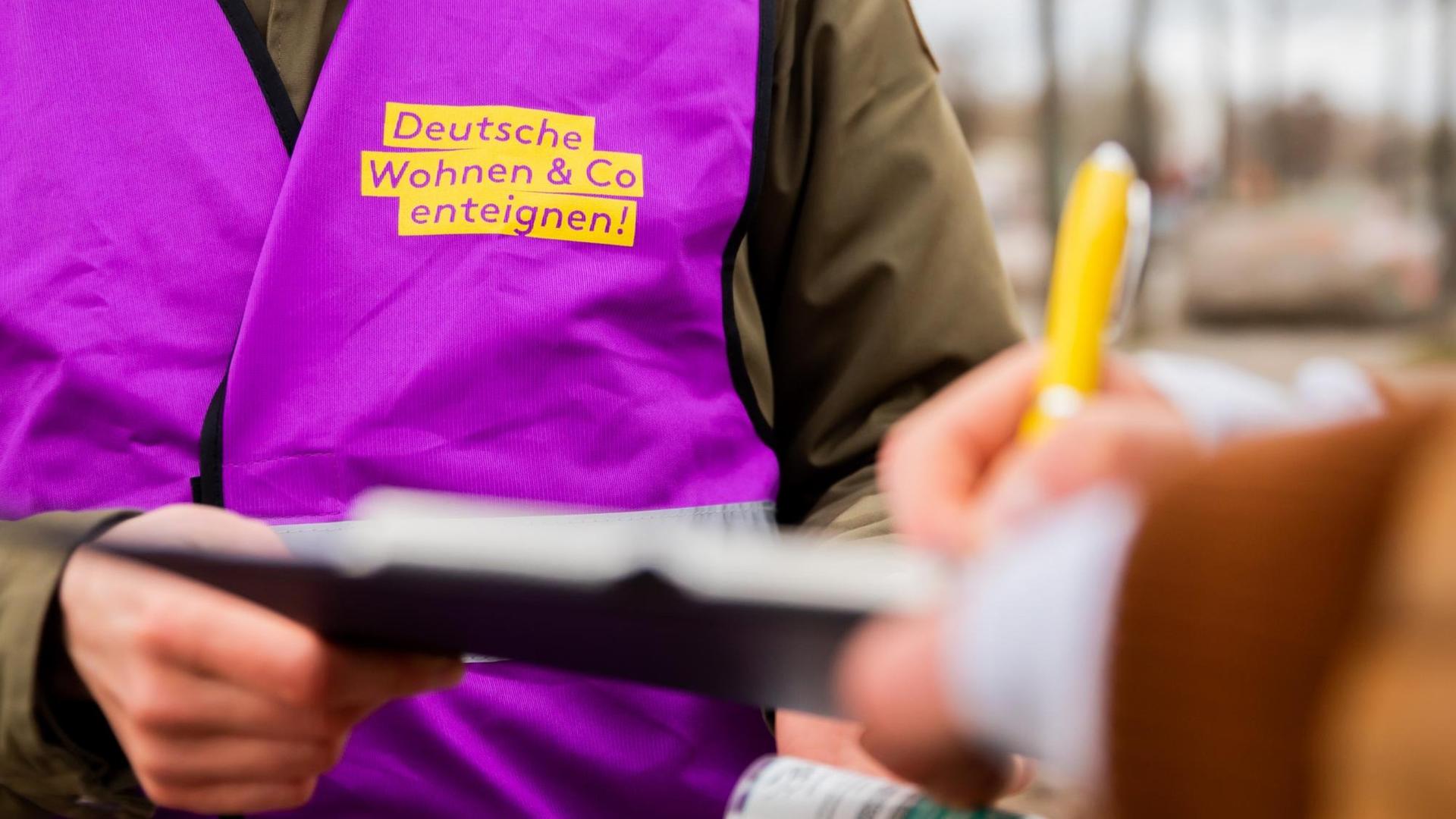 Eine Aktivistin des Volksbegehrens "Deutsche Wohnen & Co. enteignen" sammelt Unterschriften. Er hält einem Unterschreibenden ein Klemmbrett hin. Eine Aktivistin des Volksbegehrens "Deutsche Wohnen & Co. enteignen" sammelt Unterschriften. Er hält einem Unterschreibenden ein Klemmbrett hin.