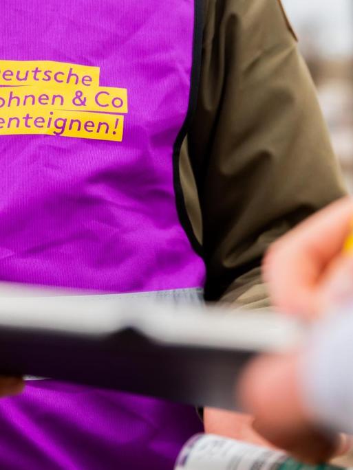 Eine Aktivistin des Volksbegehrens "Deutsche Wohnen & Co. enteignen" sammelt Unterschriften. Er hält einem Unterschreibenden ein Klemmbrett hin.