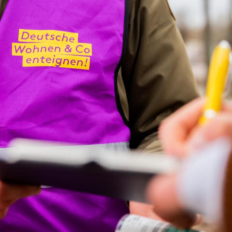 Eine Aktivistin des Volksbegehrens "Deutsche Wohnen & Co. enteignen" sammelt Unterschriften. Er hält einem Unterschreibenden ein Klemmbrett hin. Eine Aktivistin des Volksbegehrens "Deutsche Wohnen & Co. enteignen" sammelt Unterschriften. Er hält einem Unterschreibenden ein Klemmbrett hin.