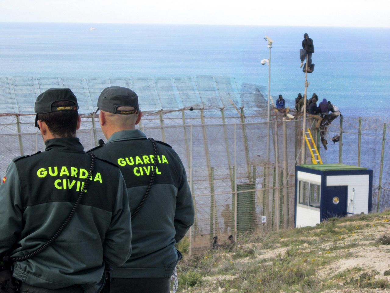 Polizisten der spanischen Guardia Civil beobachten, wie afrikanische Flüchtlinge den Grenzzaun zur spanischen Exklave Melilla überwinden