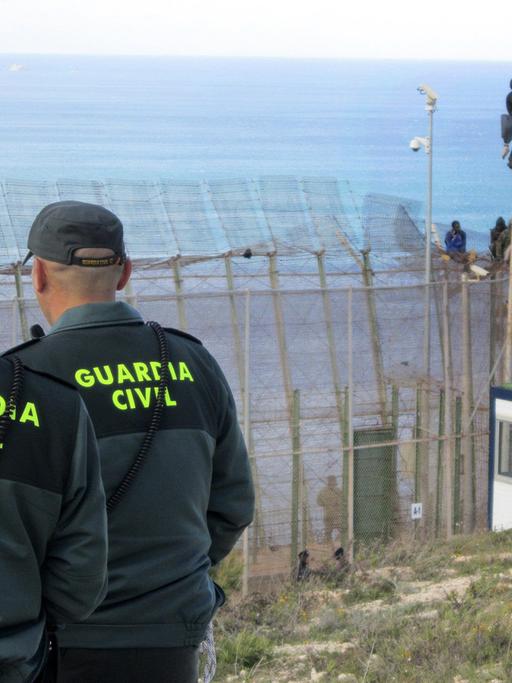 Polizisten der spanischen Guardia Civil beobachten, wie afrikanische Flüchtlinge den Grenzzaun zur spanischen Exklave Melilla überwinden
