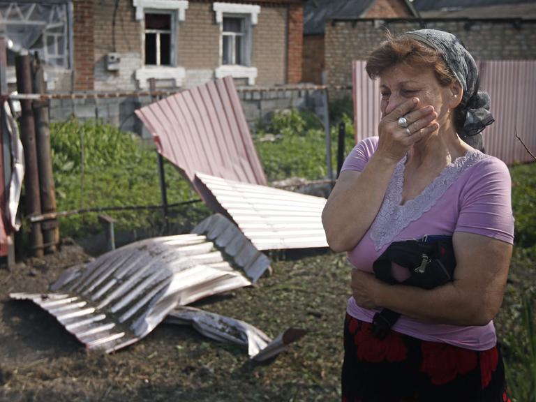 Eine Frau steht trauernd vor ihrem von Kämpfen zerstörten Anwesen.