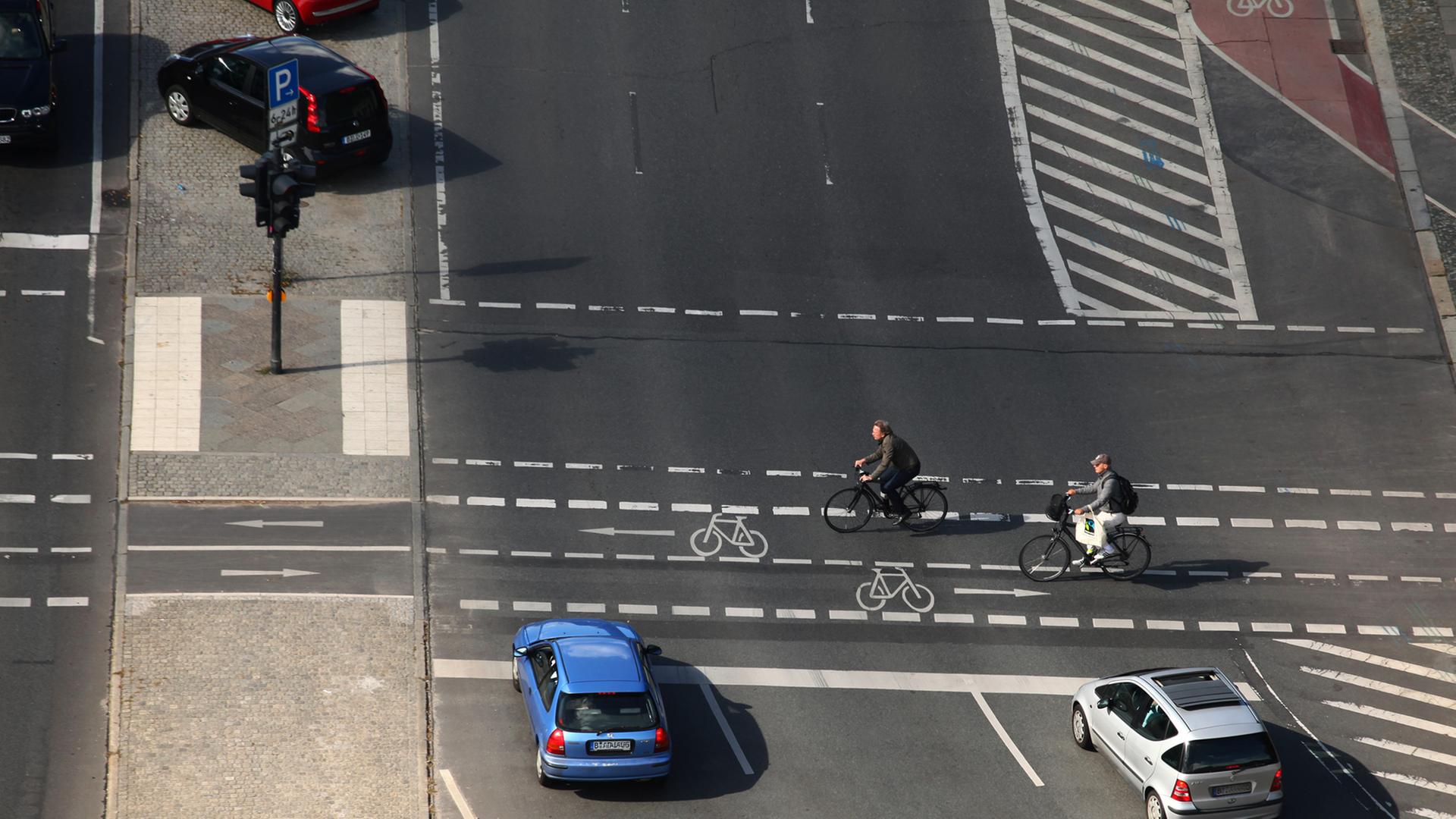 Zwei Radfahrer überqueren eine Kreuzung an einer Hauptstraße in Berlin.