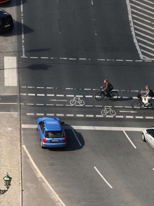 Zwei Radfahrer überqueren eine Kreuzung an einer Hauptstraße in Berlin.