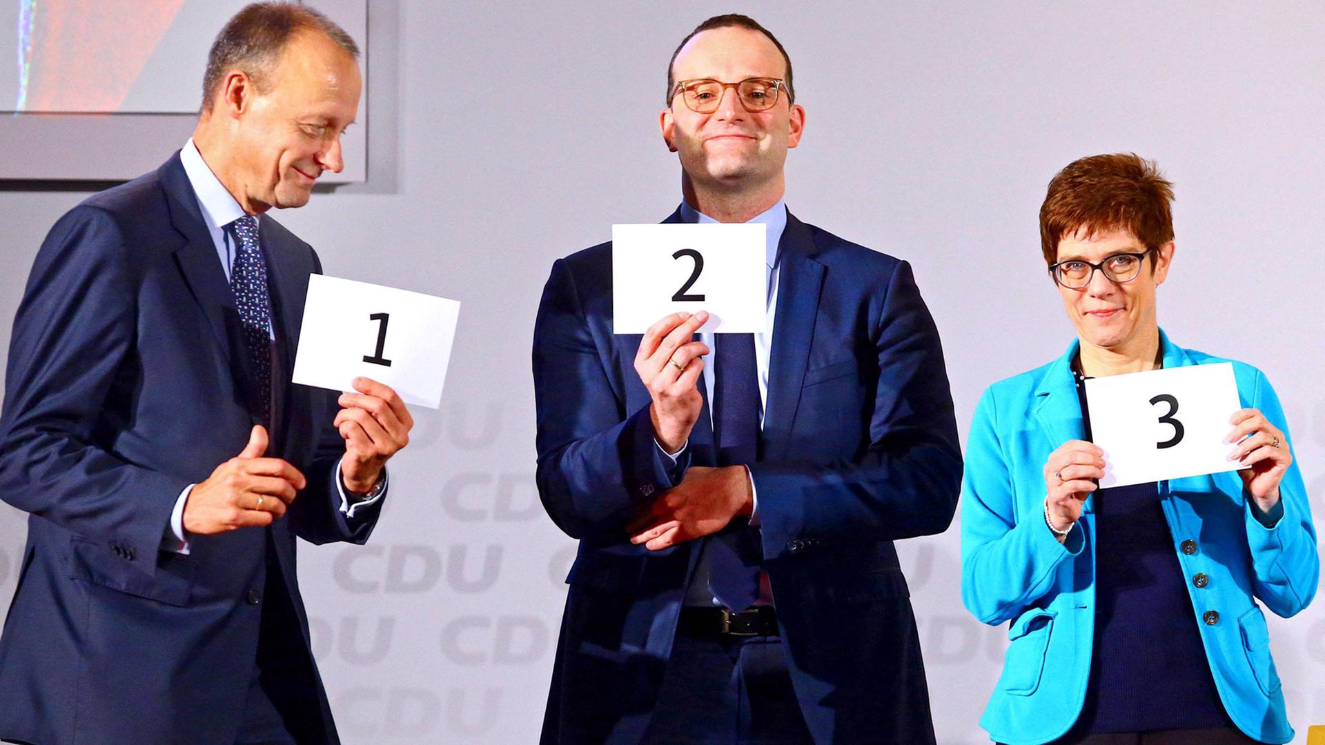 Friedrich Merz, Jens Spahn und Annegret Kramp Karrenbauer halten Zettel mit Zahlen in die Höhe.